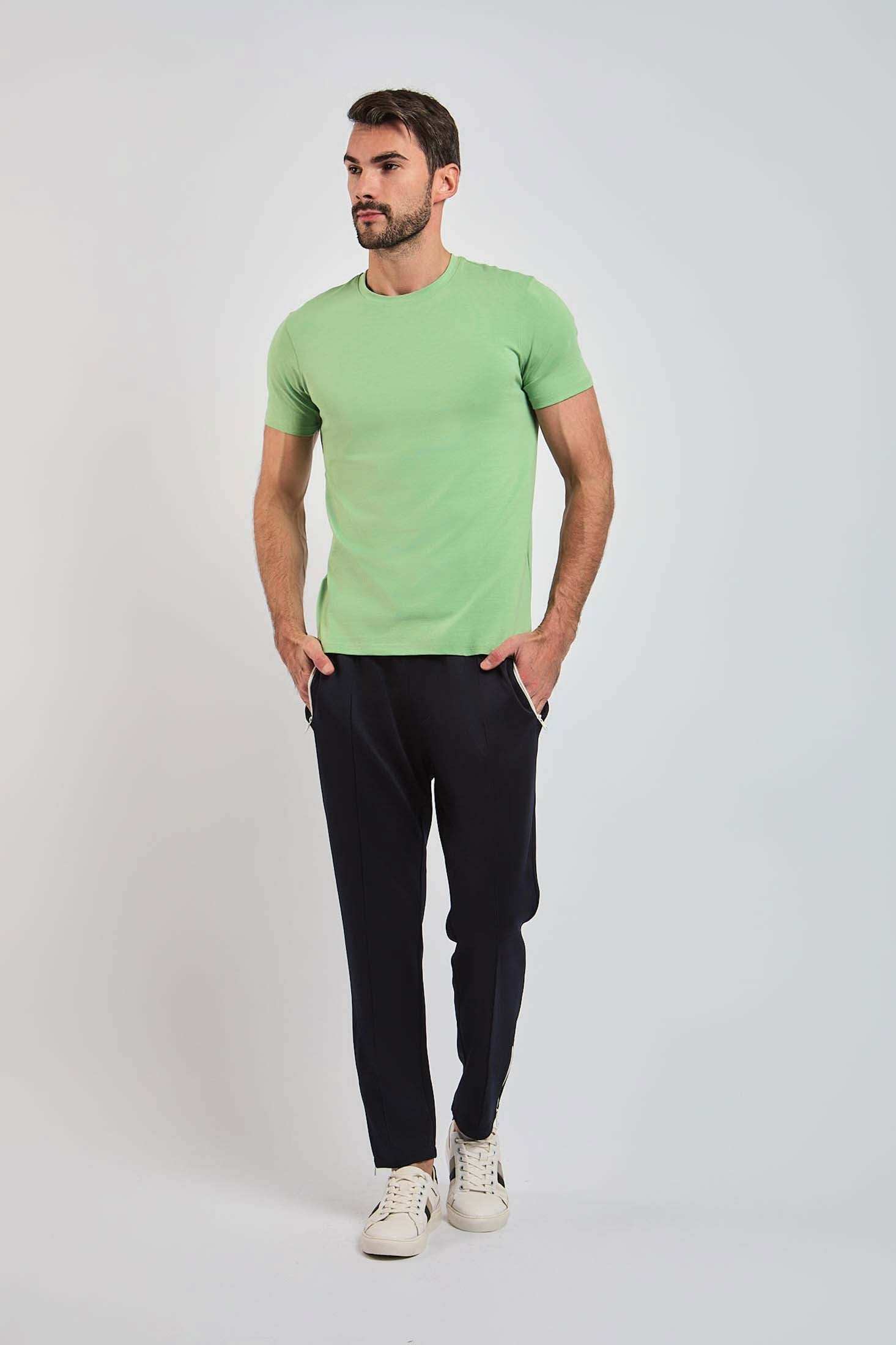 Man wearing light green t-shirt, black pants, and white sneakers on plain background
