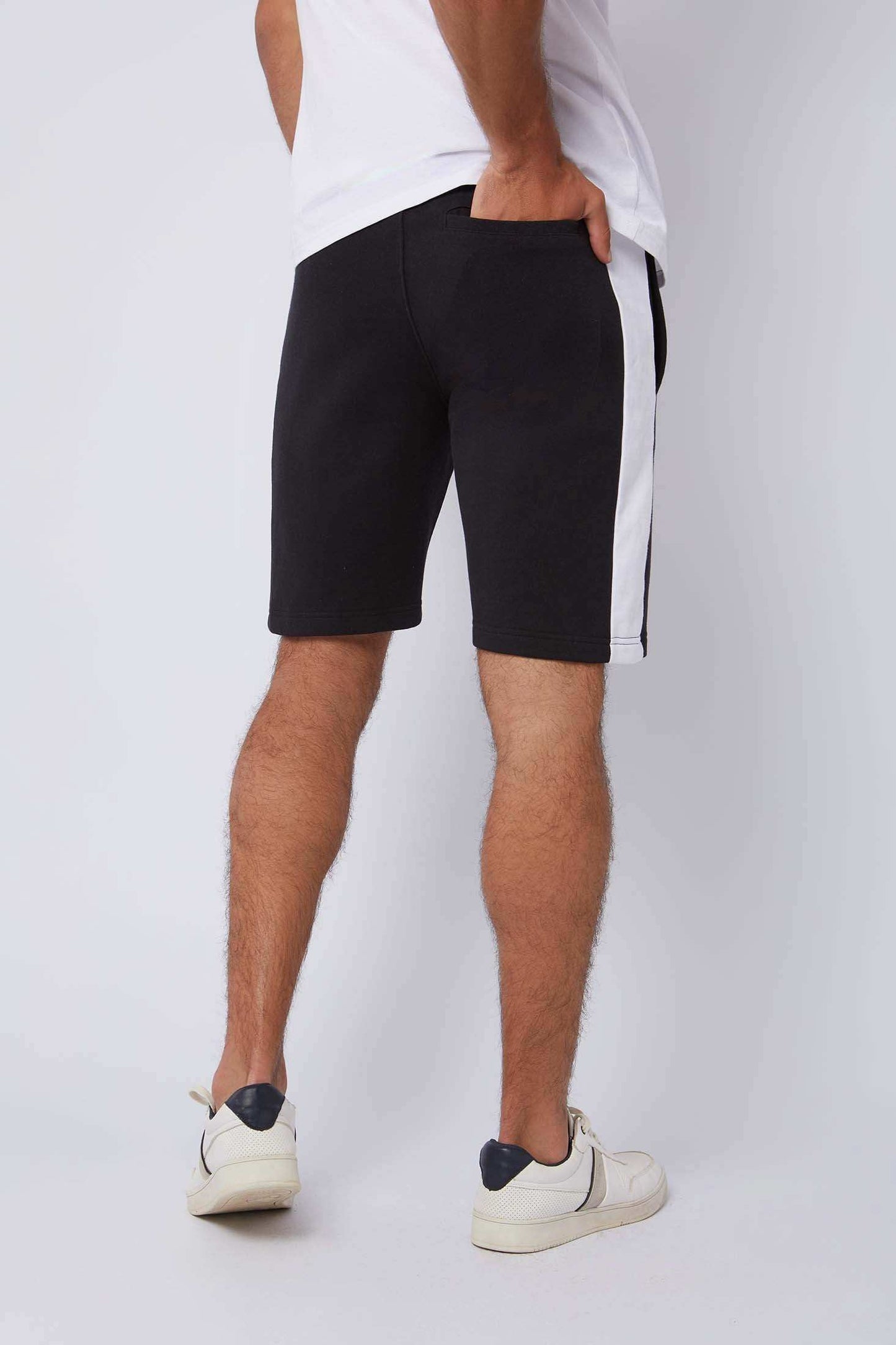 Men's black shorts with white side stripe, white sneakers, and white t-shirt, rear view