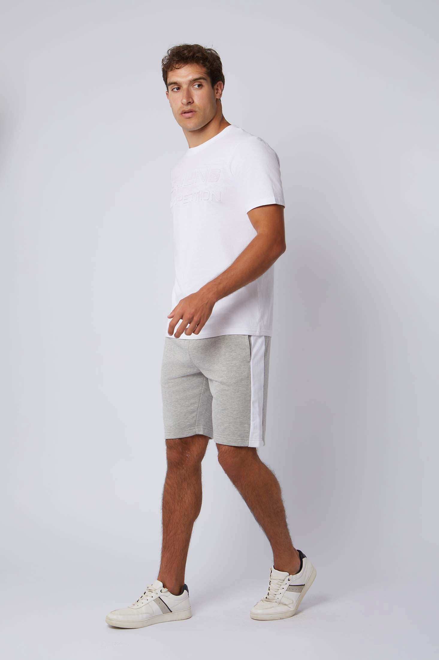 Man wearing white t-shirt, gray athletic shorts and sneakers on plain background