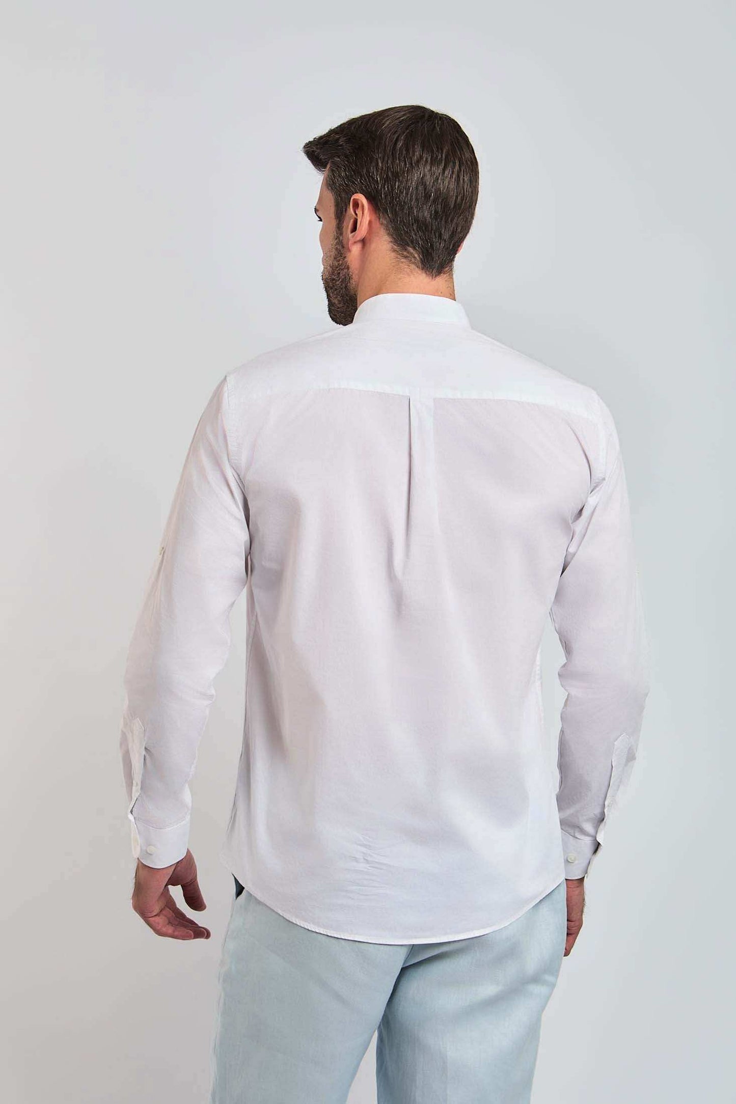 Man in white long sleeve shirt and light pants, back view, plain background