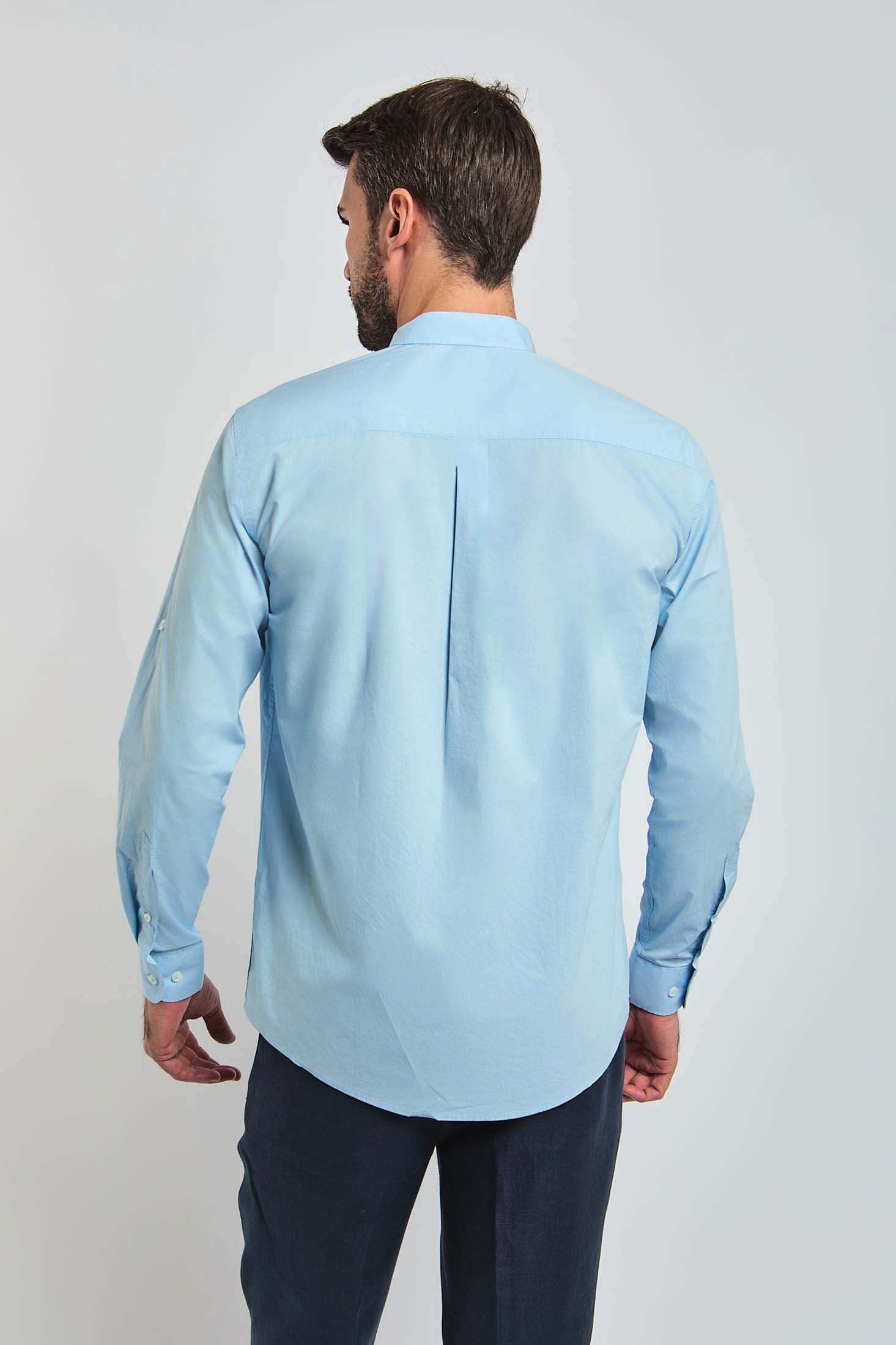 Man wearing a light blue long sleeve dress shirt, back view, with dark trousers, against plain background.