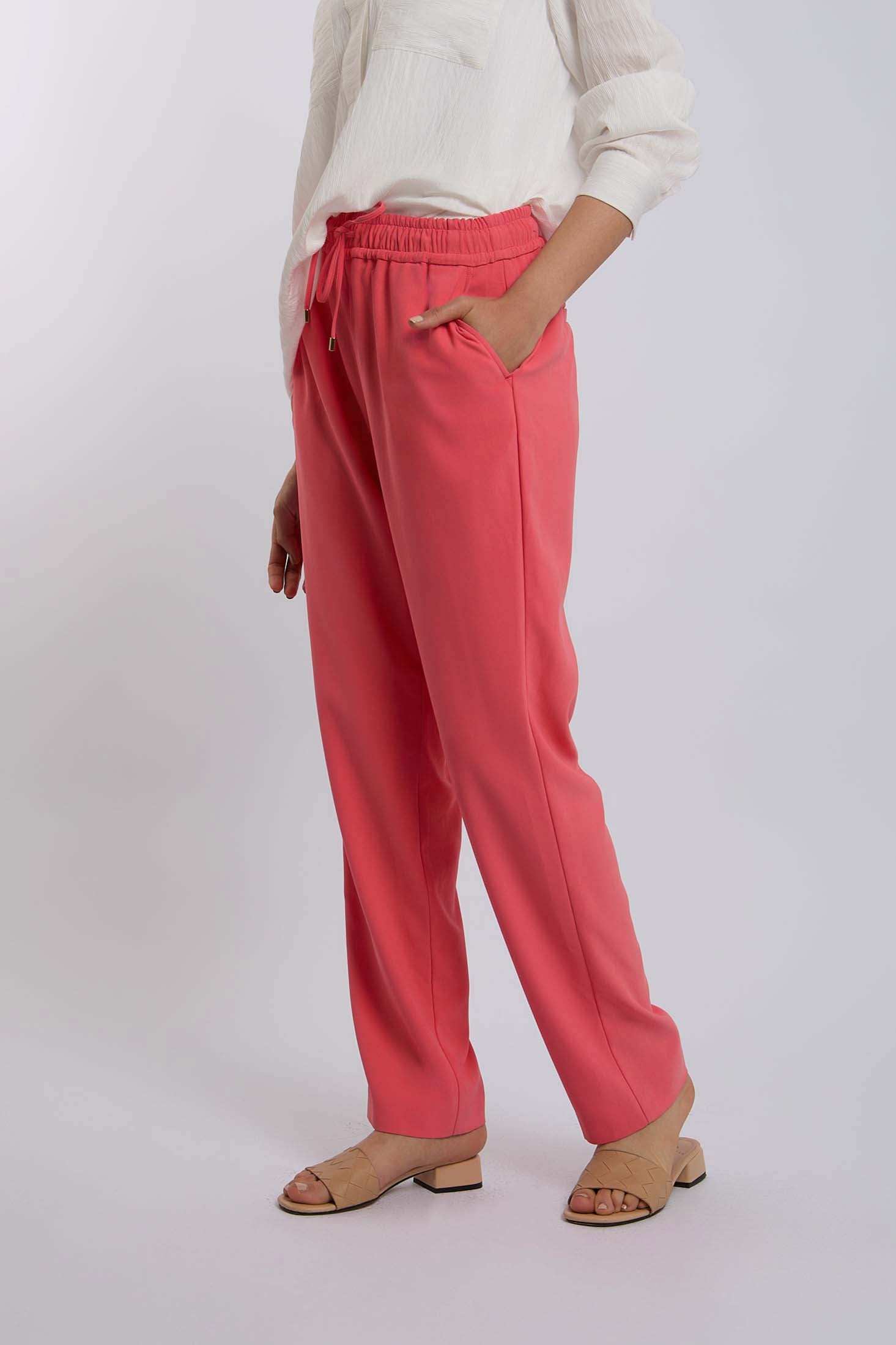 Woman wearing coral pink drawstring pants with side pockets and beige heeled sandals