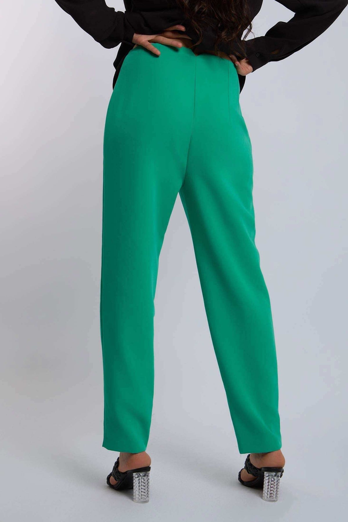 Woman wearing high-waisted green trousers and black heels, rear view