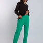 Woman in black blouse and green tailored pants with black heeled sandals, studio background