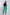 Woman in black blouse and green tailored pants with black heeled sandals, studio background