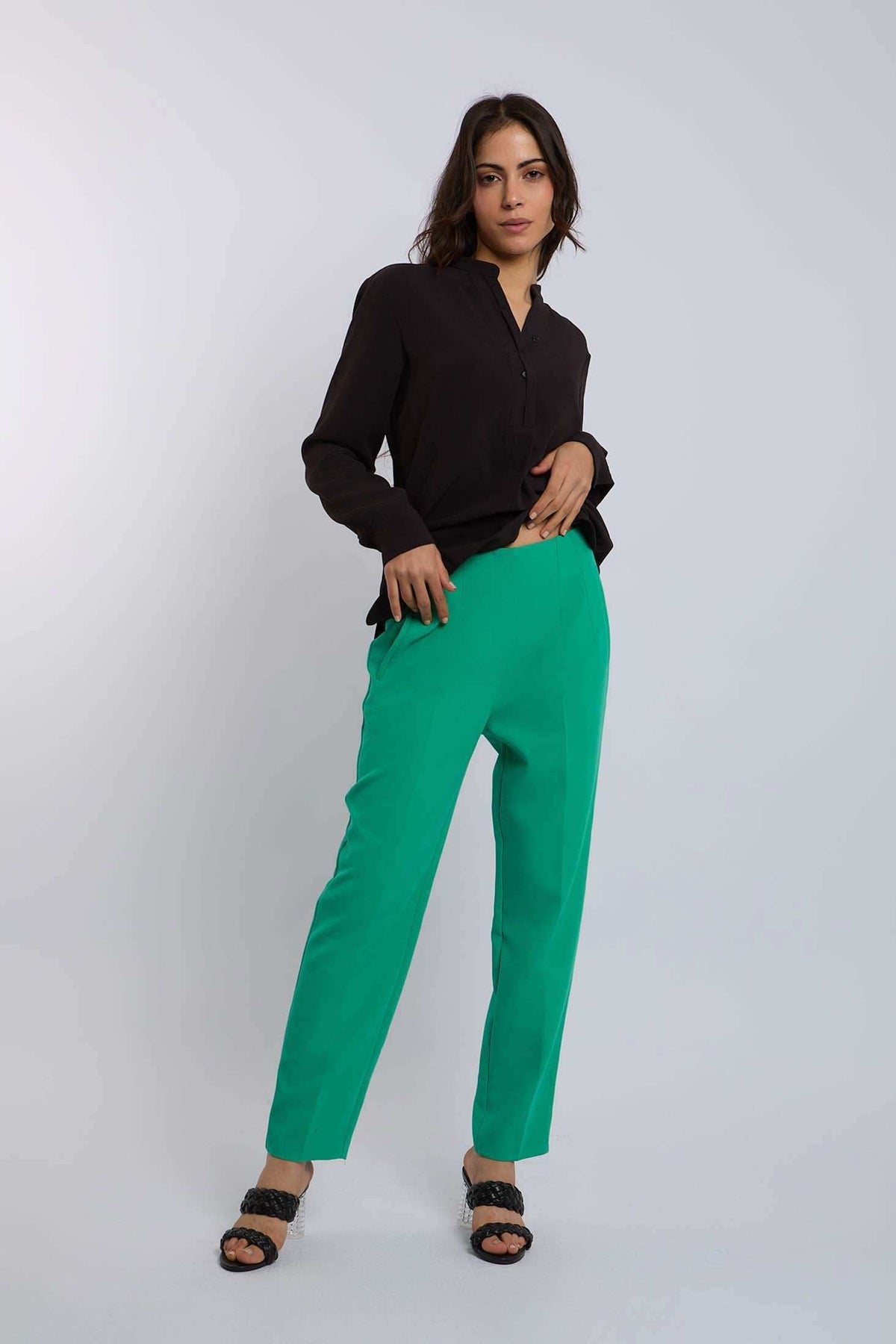 Woman in black blouse and green tailored pants with black heeled sandals, studio background