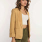 Woman in mustard yellow blazer, white crop top, and olive green pants on white background