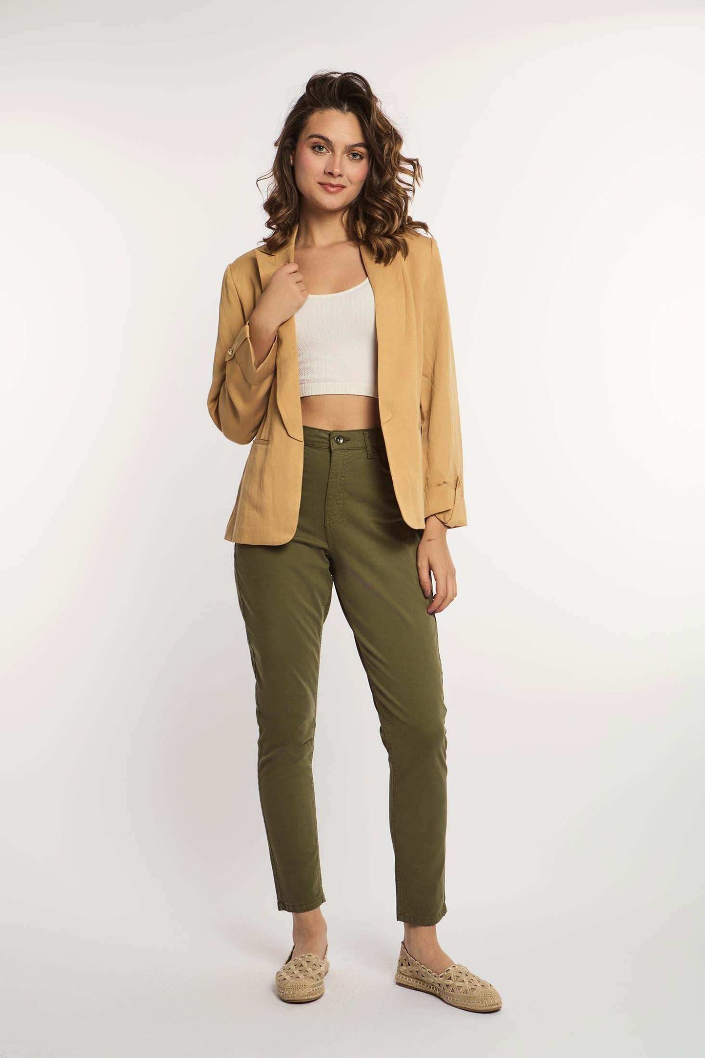 Woman wearing beige blazer, white crop top, olive green pants, and woven loafers
