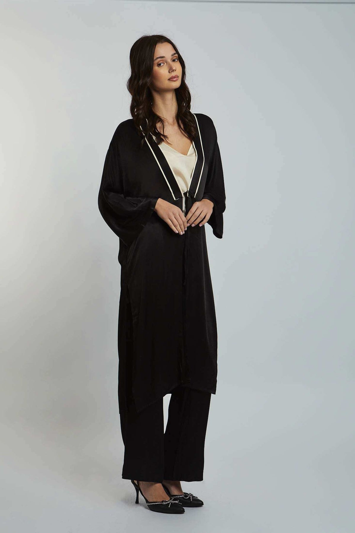 Woman wearing a black long cardigan with white trim, cream blouse, wide-leg pants, and heels
