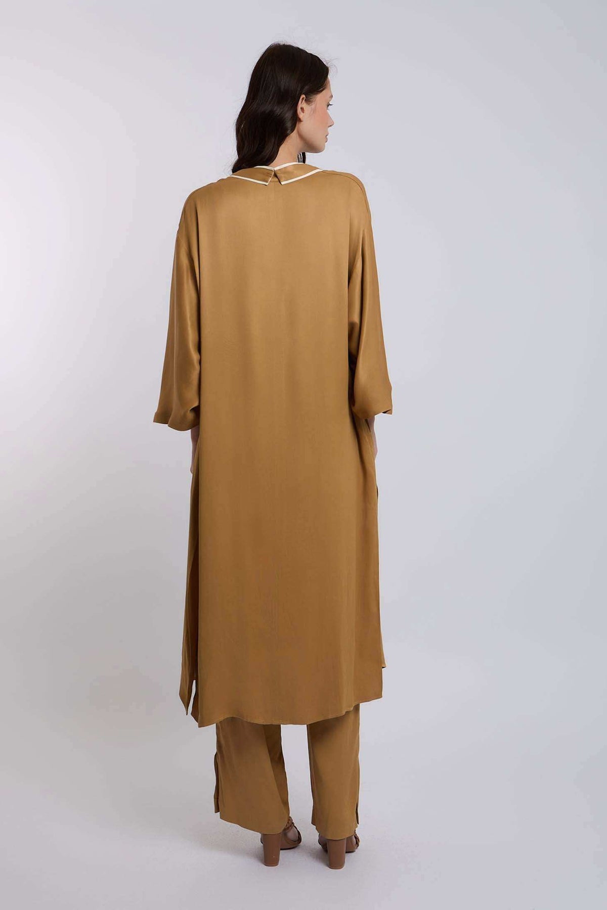 Woman wearing a loose camel brown long tunic top and matching pants, back view