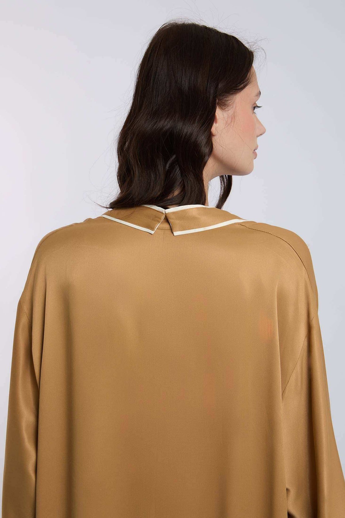 Woman wearing a satin camel blouse with white-trimmed collar, shown from the back