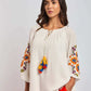 Woman wearing white embroidered peasant blouse with tassels and orange pants