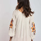Woman wearing white blouse with colorful floral embroidery on sleeves, red pants, back view