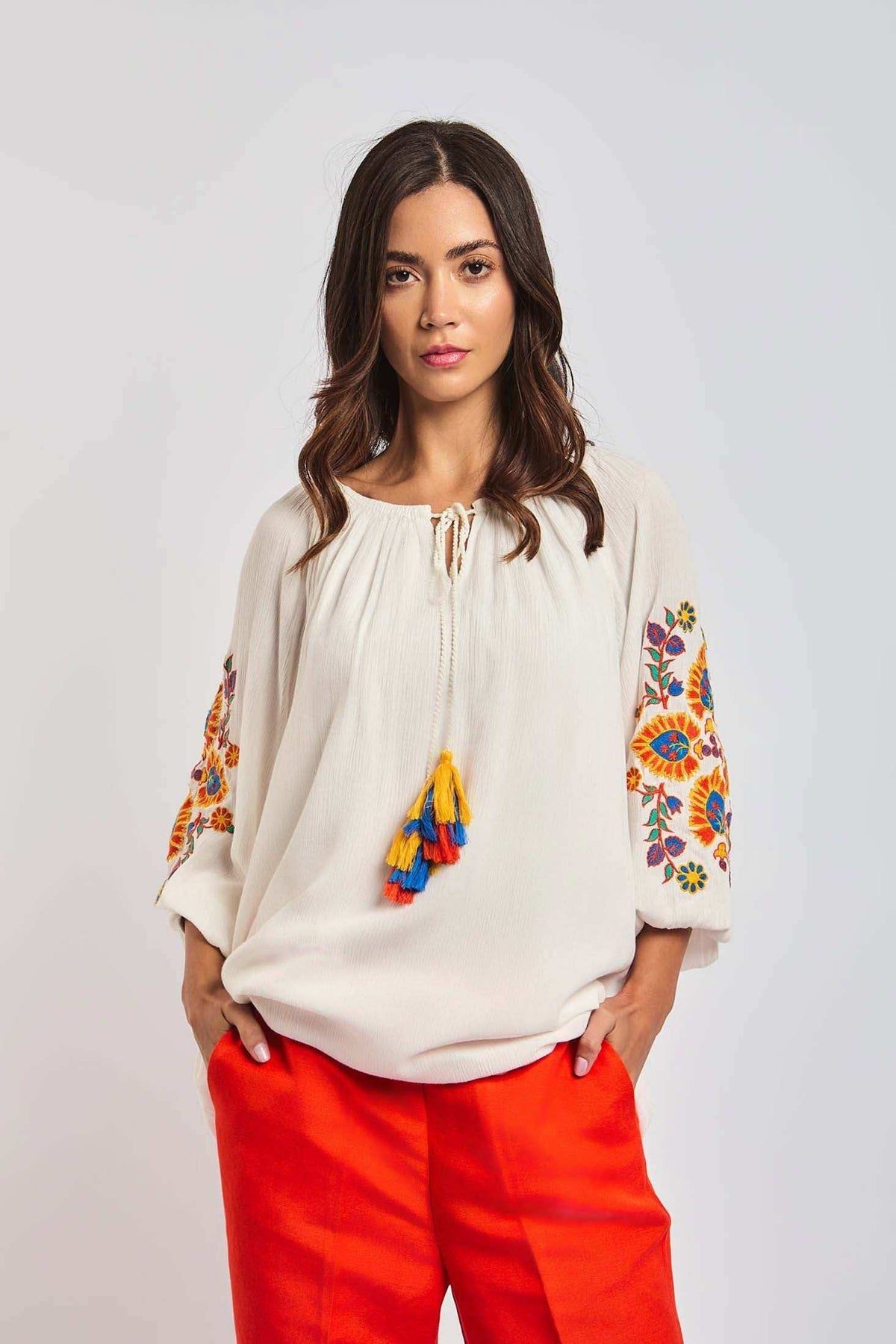 Woman wearing a white embroidered blouse with colorful tassels and bright orange pants