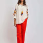 Woman wearing white embroidered blouse with tassels and bright red trousers