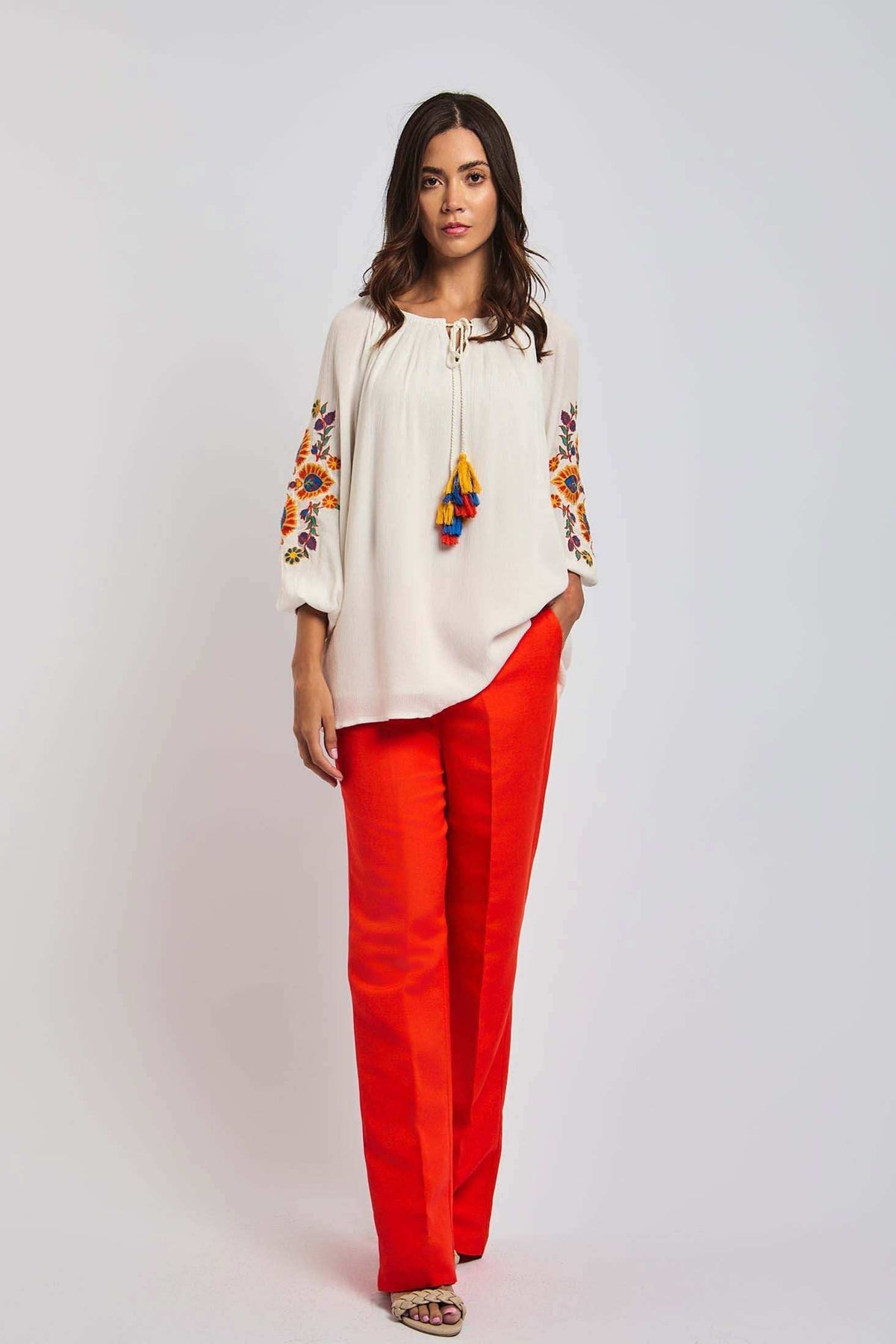 Woman wearing white embroidered blouse with tassels and bright red trousers