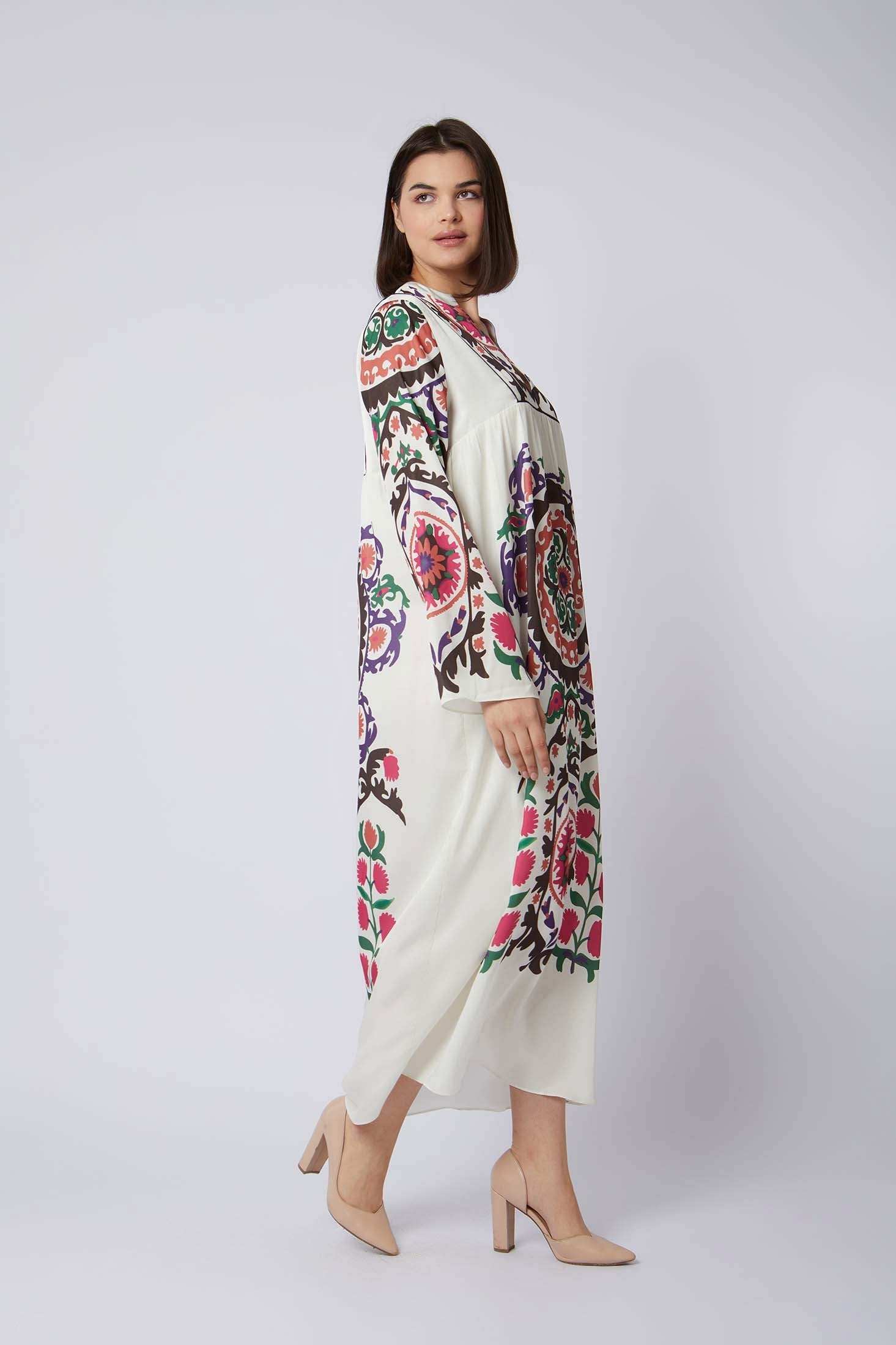 Woman wearing long white dress with vibrant multicolor floral patterns and beige heels