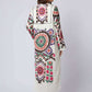 Woman wearing a long cream dress with colorful floral and geometric patterns, back view