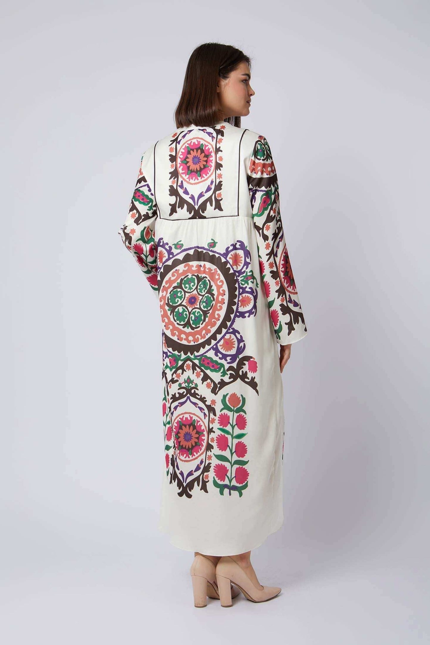 Woman wearing a long cream dress with colorful floral and geometric patterns, back view