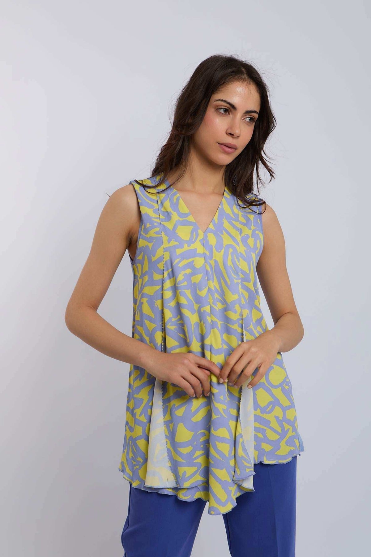Woman wearing a sleeveless yellow and blue patterned V-neck top with blue pants