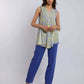 Woman wearing a sleeveless yellow and blue patterned top with blue pants and beige heels