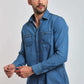 Man wearing a casual blue denim button-up shirt with chest pockets and white pants