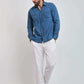 Man wearing blue denim shirt with chest pockets, white pants, and sneakers against plain background
