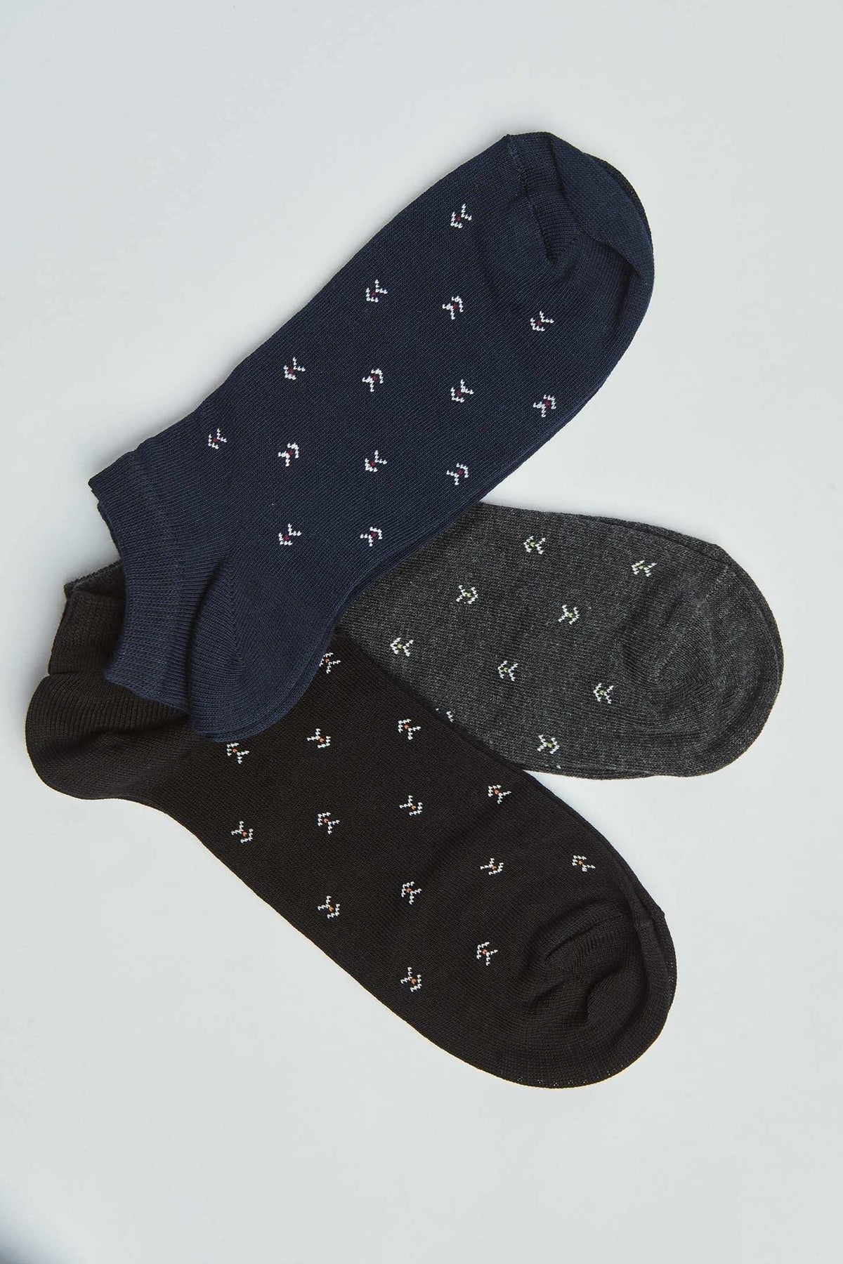 Set of three low-cut patterned socks in navy, gray, and black on a white background