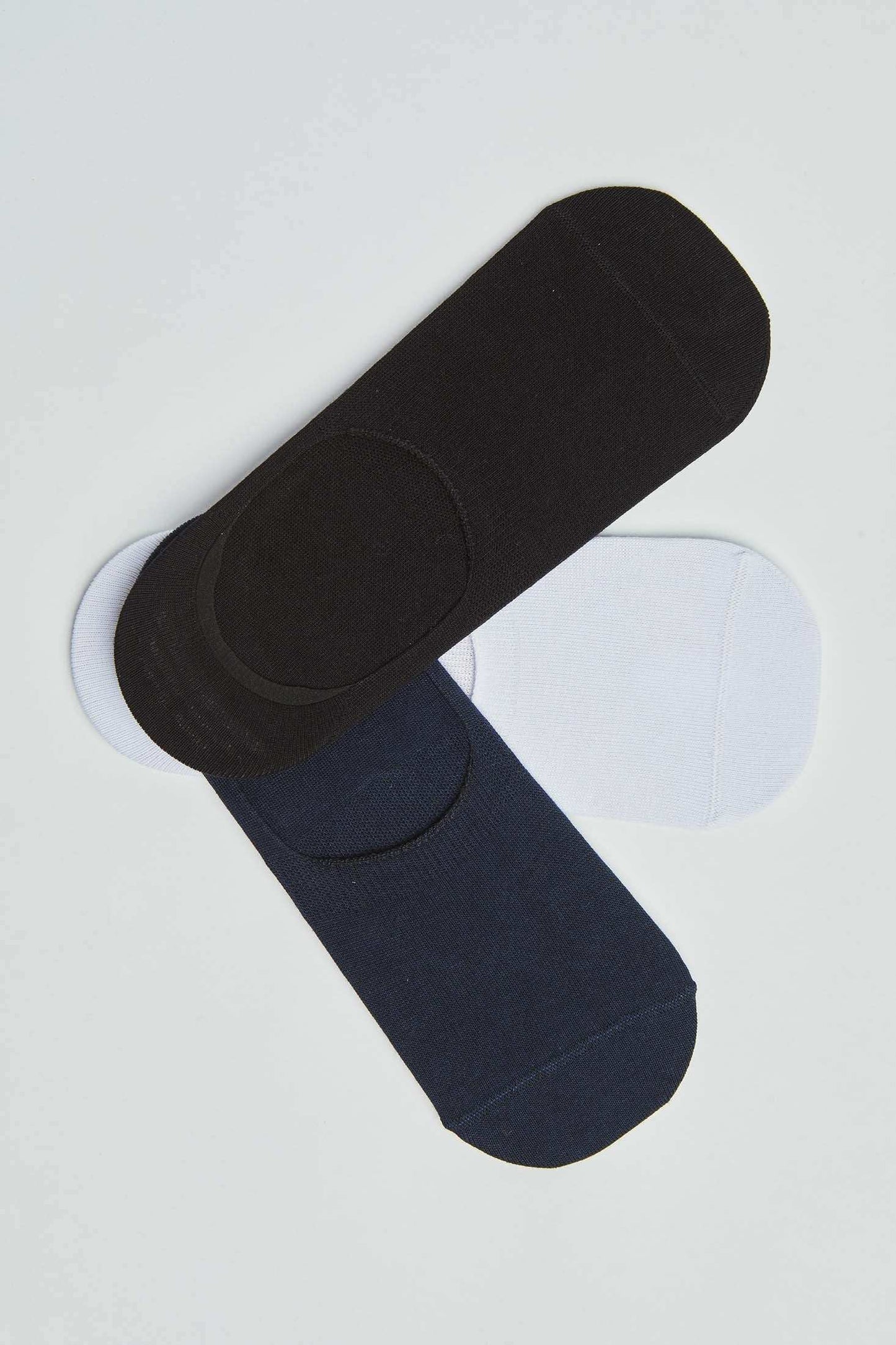 Three pairs of no show socks in black, navy, and white on a plain background