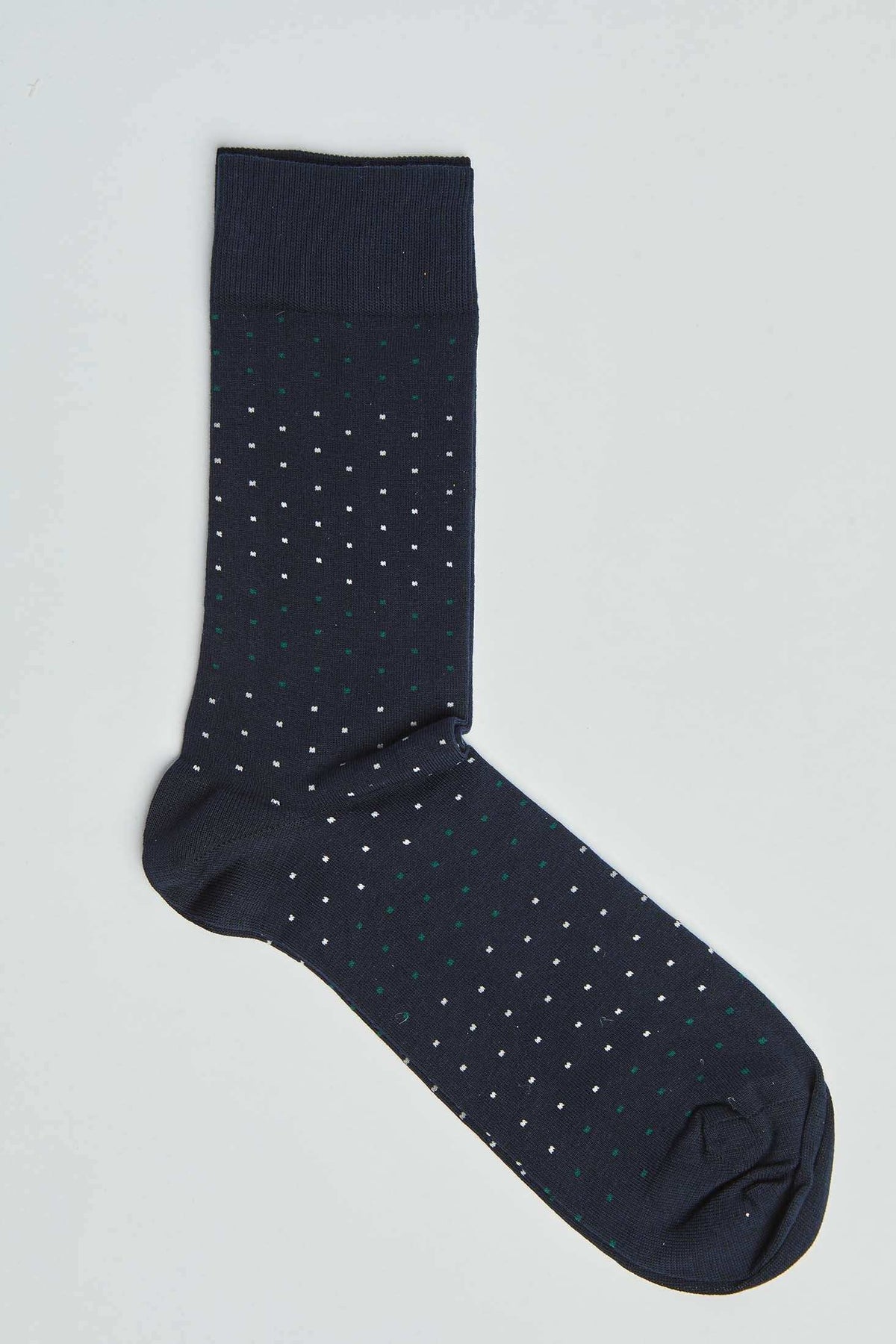 Navy blue dress sock with small white and green polka dot pattern on plain background