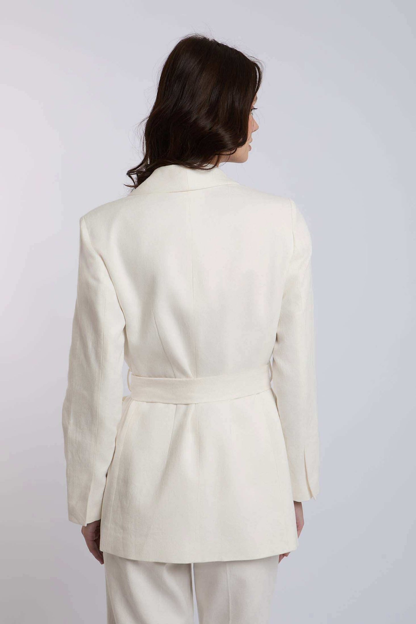 Woman wearing white belted blazer with long sleeves, back view, formal attire
