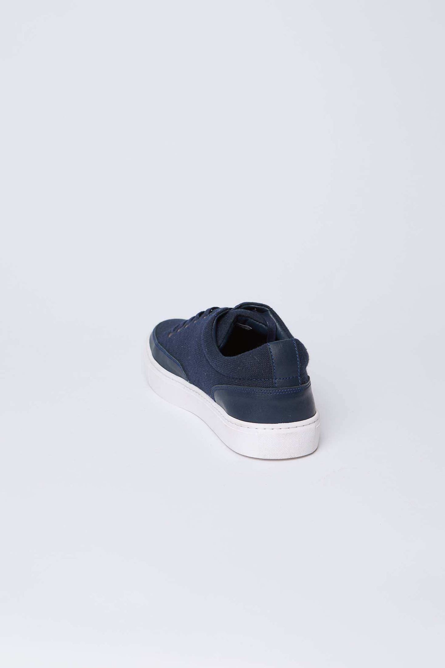 Navy blue men's casual sneaker with white sole on light background, rear angle view