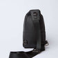 Black leather textured sling bag with adjustable strap and metallic rings on white background