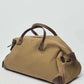 Brown canvas duffle bag with leather handles and accents on a plain background