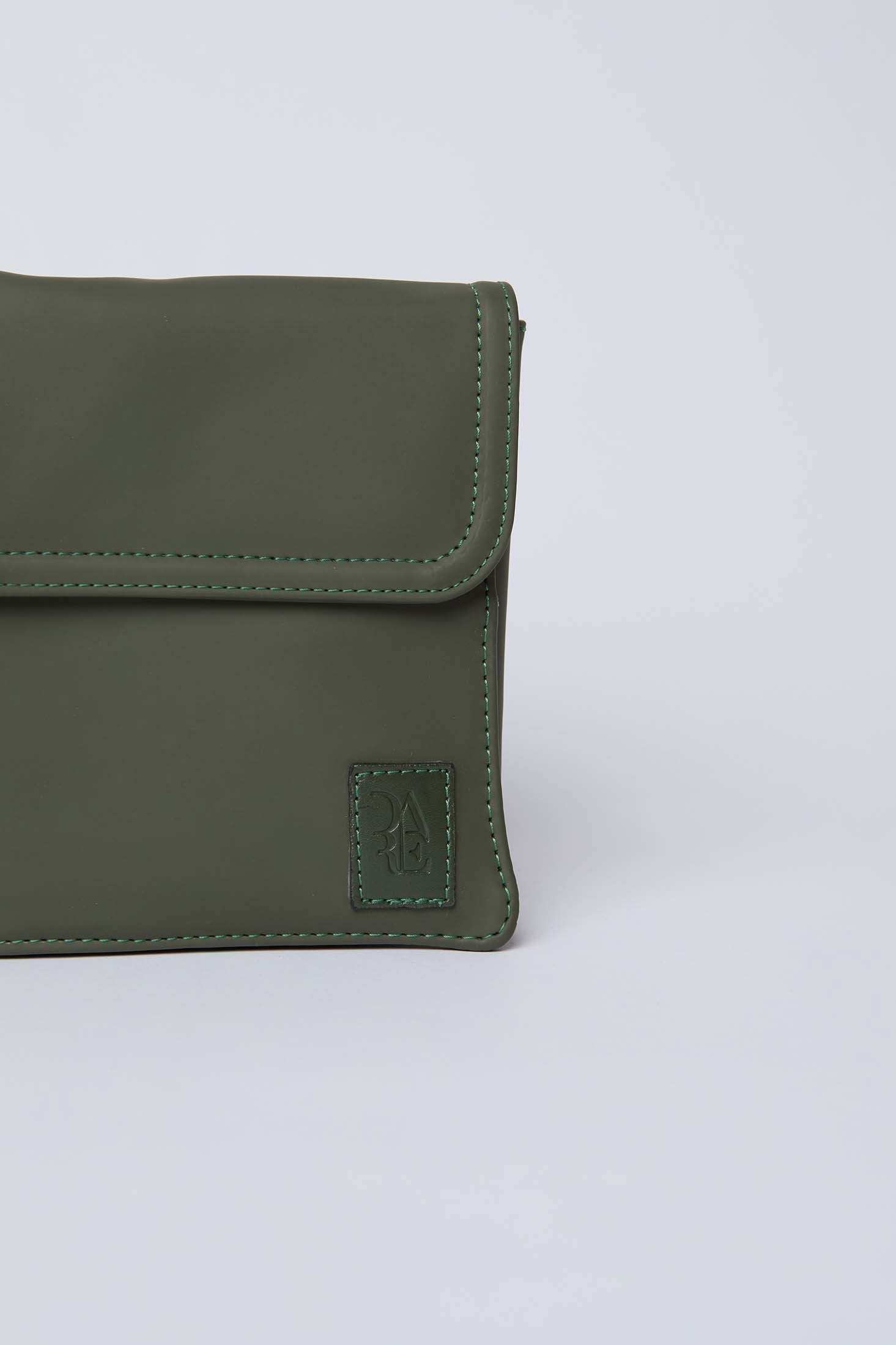 Close-up of olive green leather crossbody bag with flap and stitched edges on light background