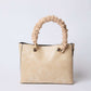 Beige textured handbag with ruched handle and gold hardware on white background