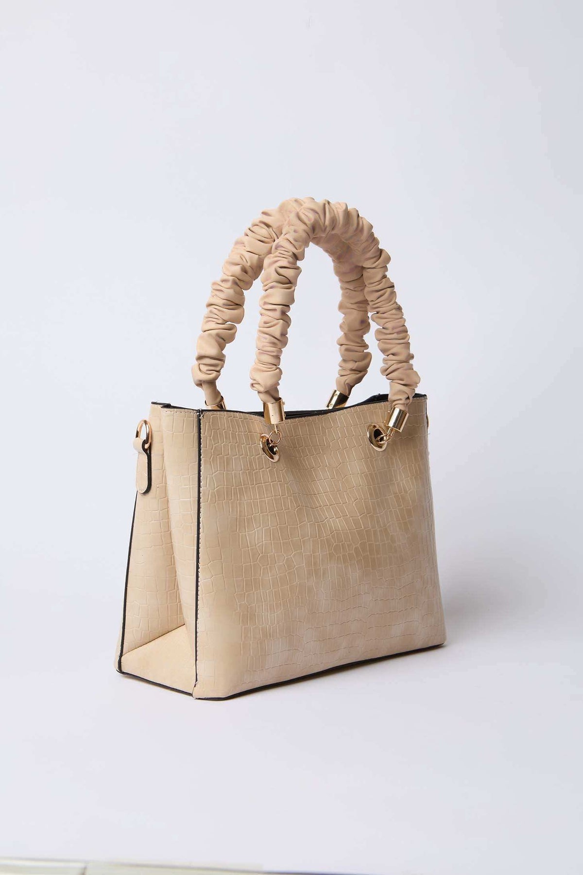Beige textured handbag with ruched handles and gold hardware on a plain background