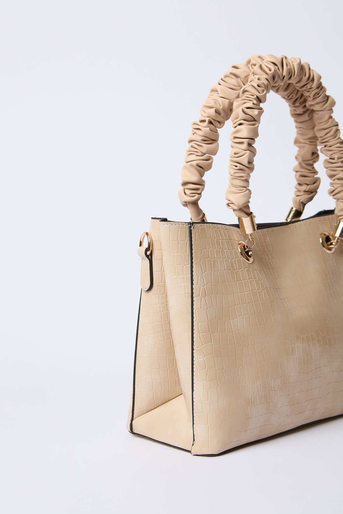 Beige textured handbag with ruched handles and gold hardware on white background