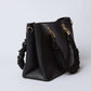 Black textured handbag with ruched handle and gold hardware on white background