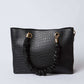 Black faux crocodile handbag with gold-tone rings and ruched handle on a white background