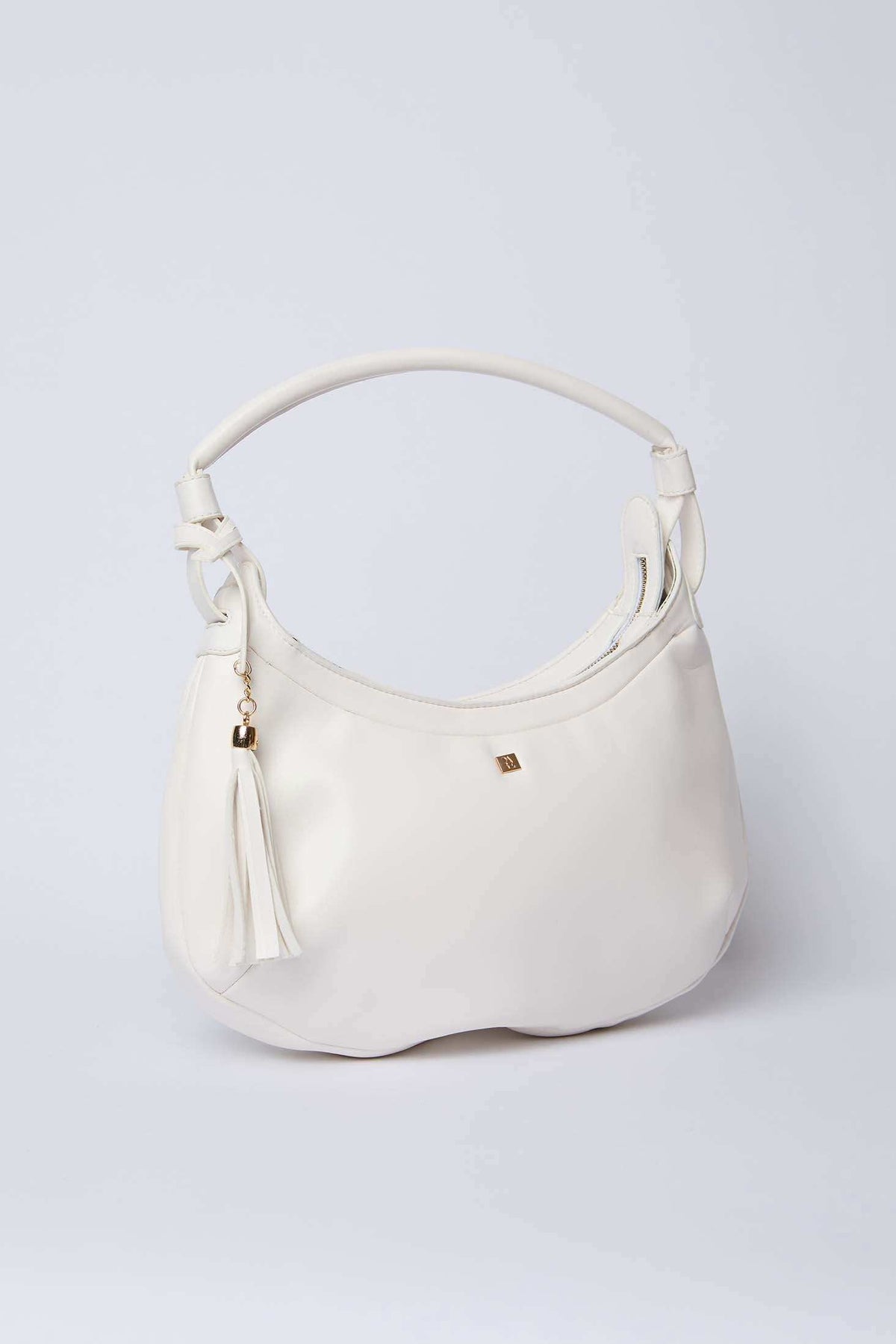 White leather handbag with tassel charm and gold-tone accent on plain background