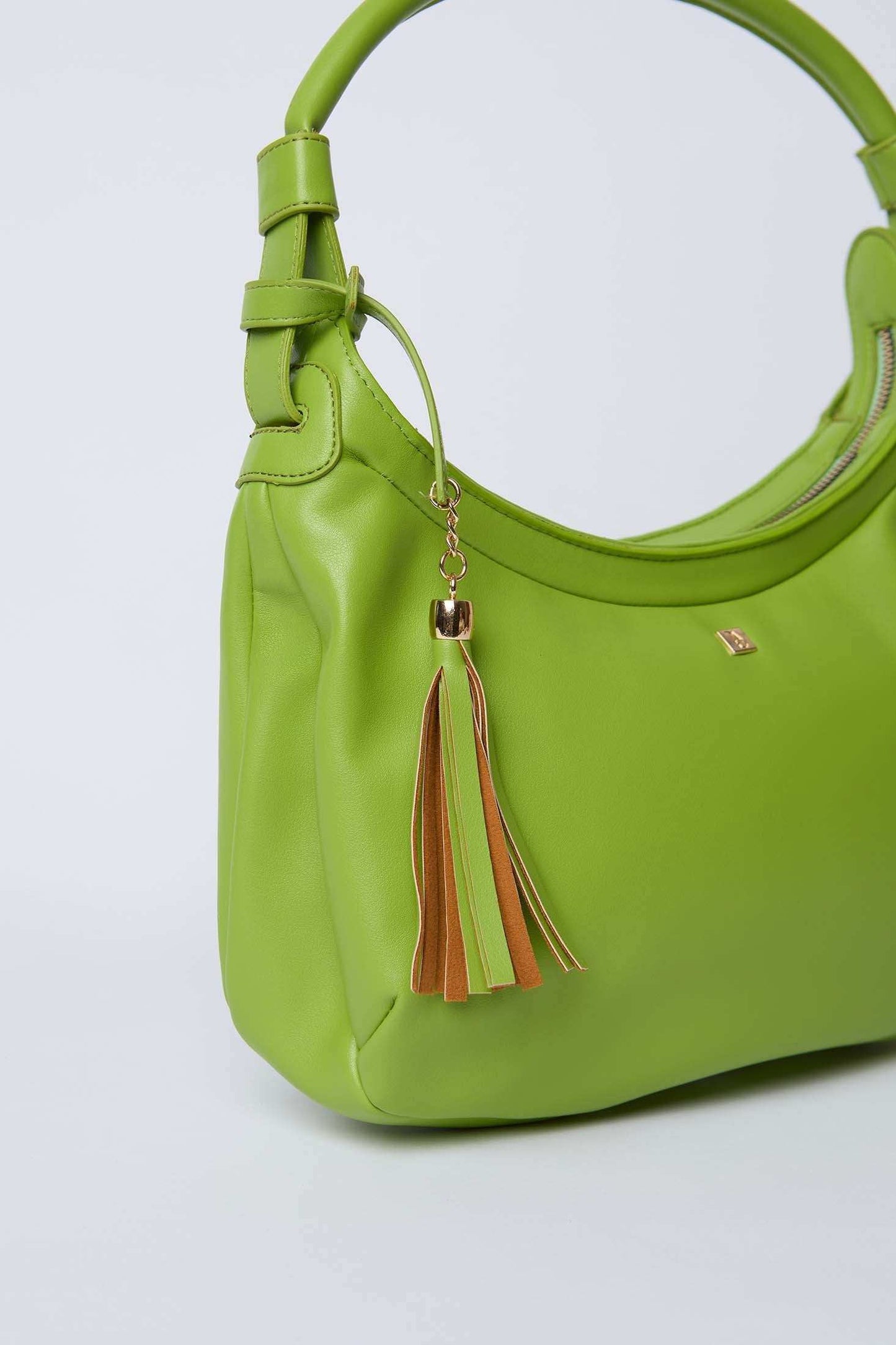 Green women's handbag with top handle and brown tassel keychain, minimalist style