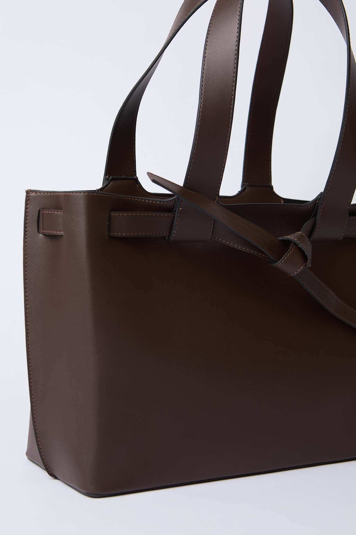 Close-up of brown leather tote bag with double handles and knotted detail on side