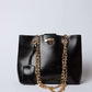 Dalydress black leather handbag with gold chain straps and tag on white background