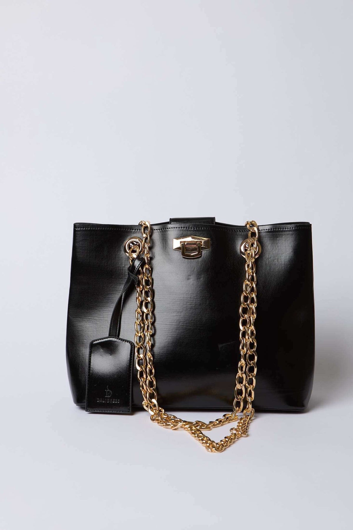 Dalydress black leather handbag with gold chain straps and tag on white background